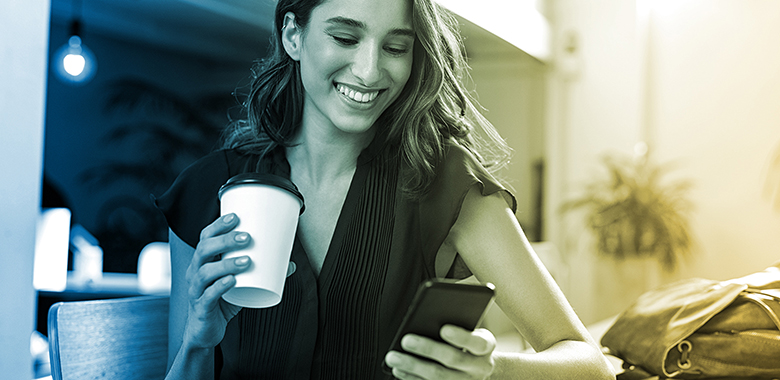 A young woman holding a coffee cup checks her phone.