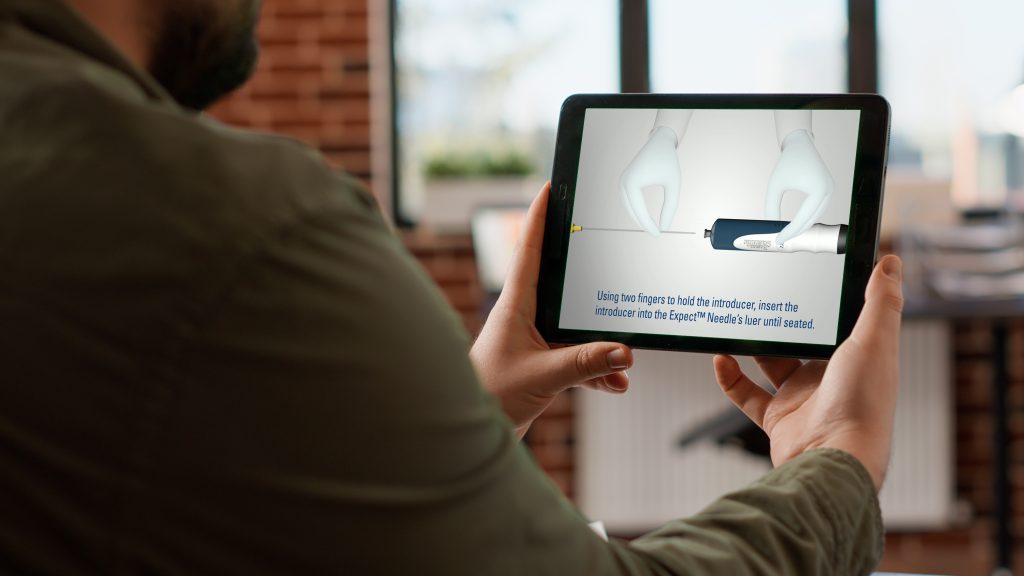 Over the shoulder view of male subject watching a medical device instructional video produced by Brella Productions on a tablet.