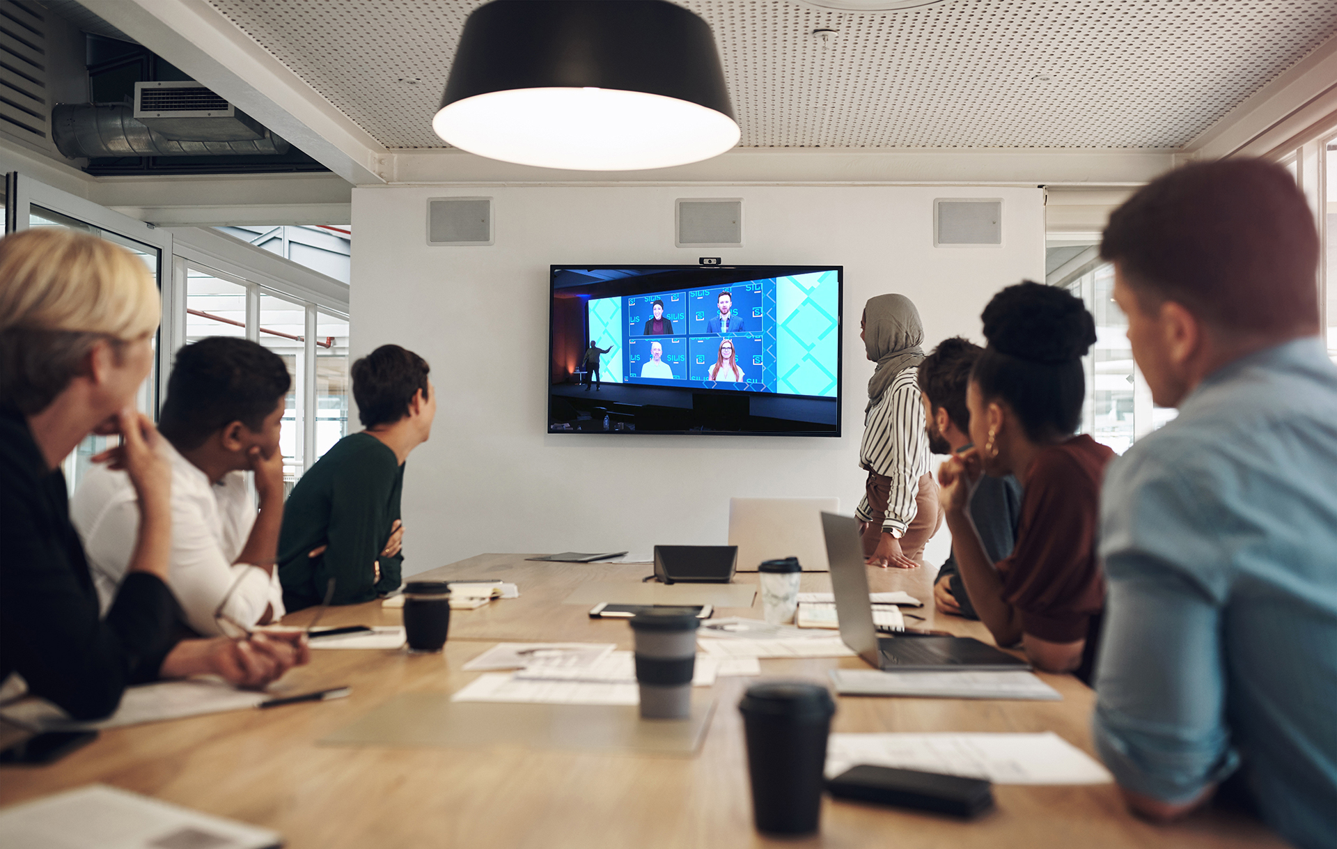 Coworkers gathered around conference table watching a virtual meeting presentation.
