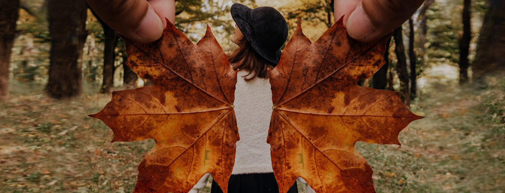 Woman in hat viewed from behind. Giant fingers hold two leaves in place as wings.