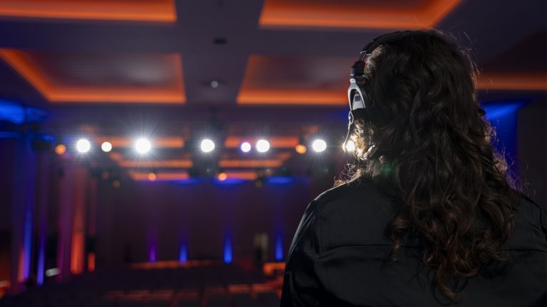 Back of house view featuring a female Brella event management agency producer looking out over darkened conference room with orange and blue accent lights.