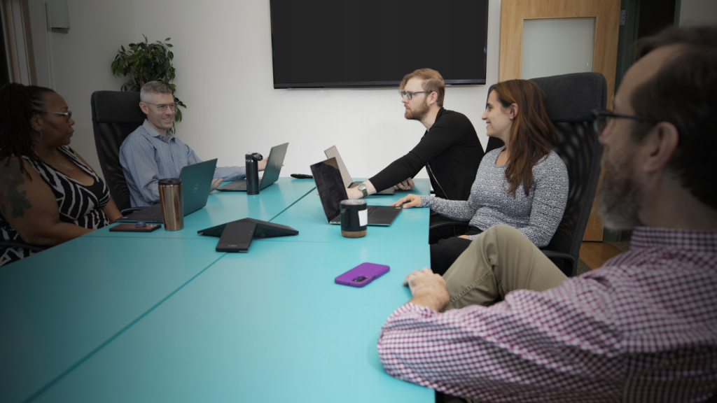 Three male and two female Brella event management agency coworkers gathered around a blue conference table.