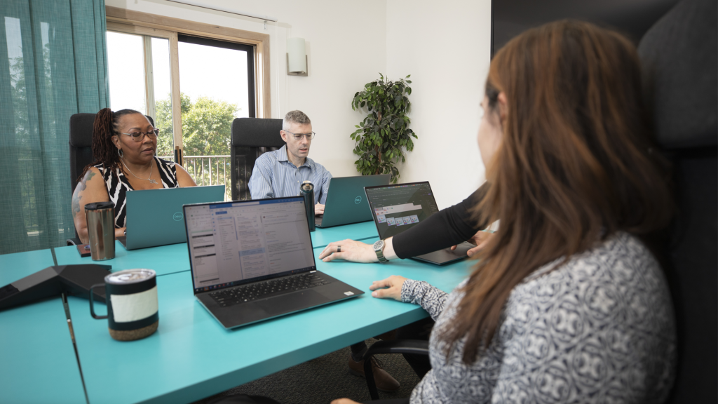 A Brella event management agency team meeting in a brightly lit conference room with trees visible through background window.