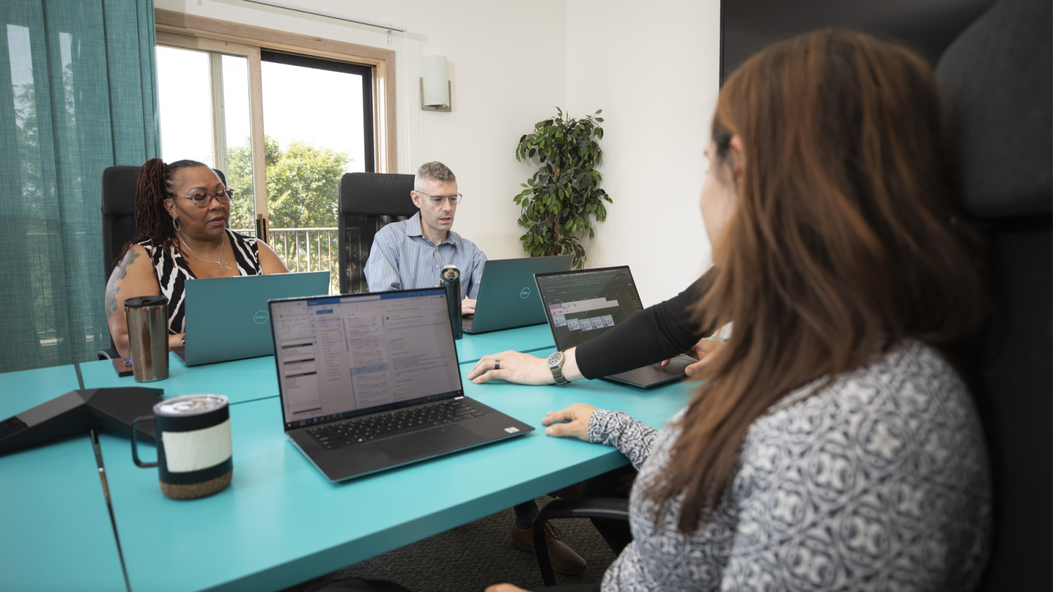 A Brella event management agency team meeting in a brightly lit conference room with trees visible through background window.
