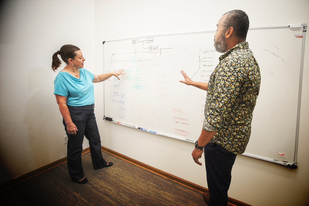 Bernadette Burke, Brella's President and Executive Learning Strategist, has a discussion in front of a whiteboard with a coworker.