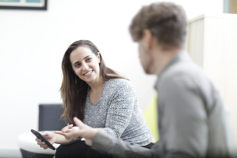Smiling, female, Brella event management agency project manager listens as a male colleague speaks.