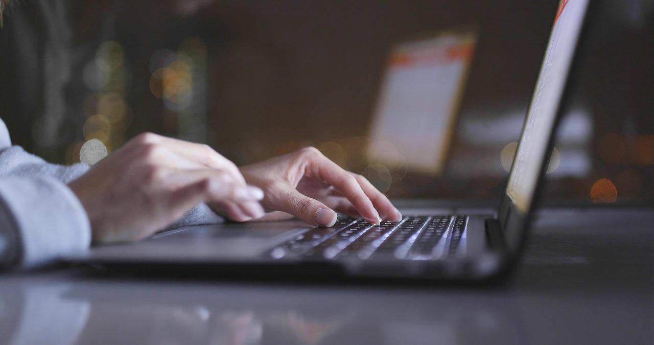 Closeup of slim-fingered hands typing on a laptop.