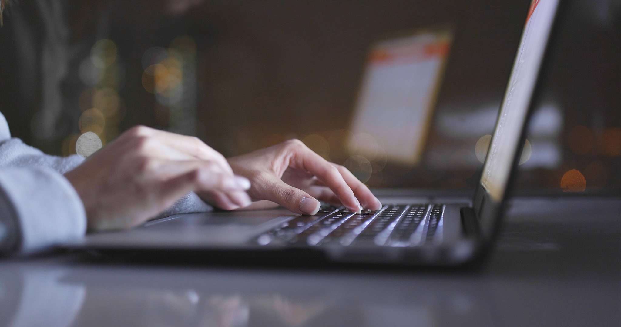 Closeup of slim-fingered hands typing on a laptop.