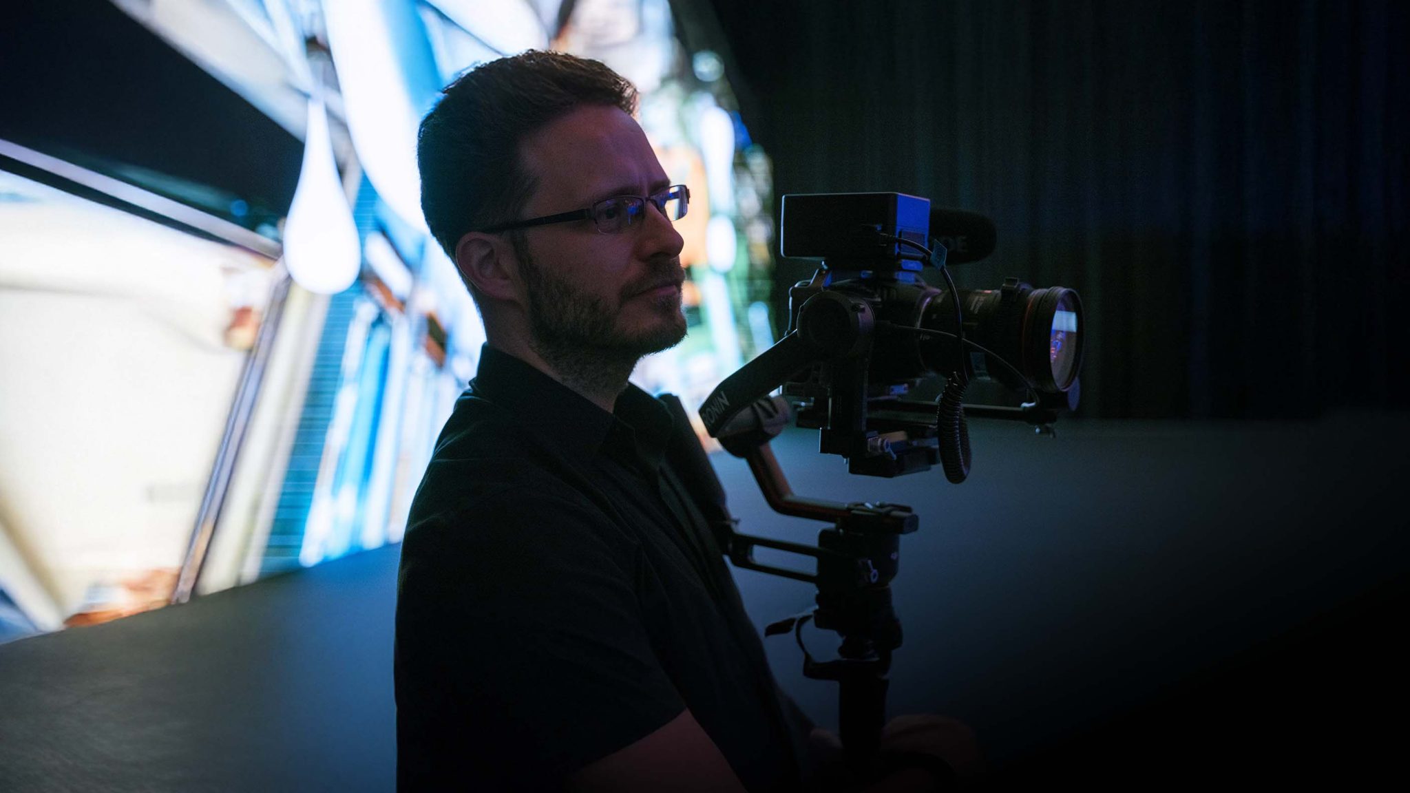 A video camera operator captures audience footage from the corner of a brightly backlit stage during a coporate event produced by Brella Productions.