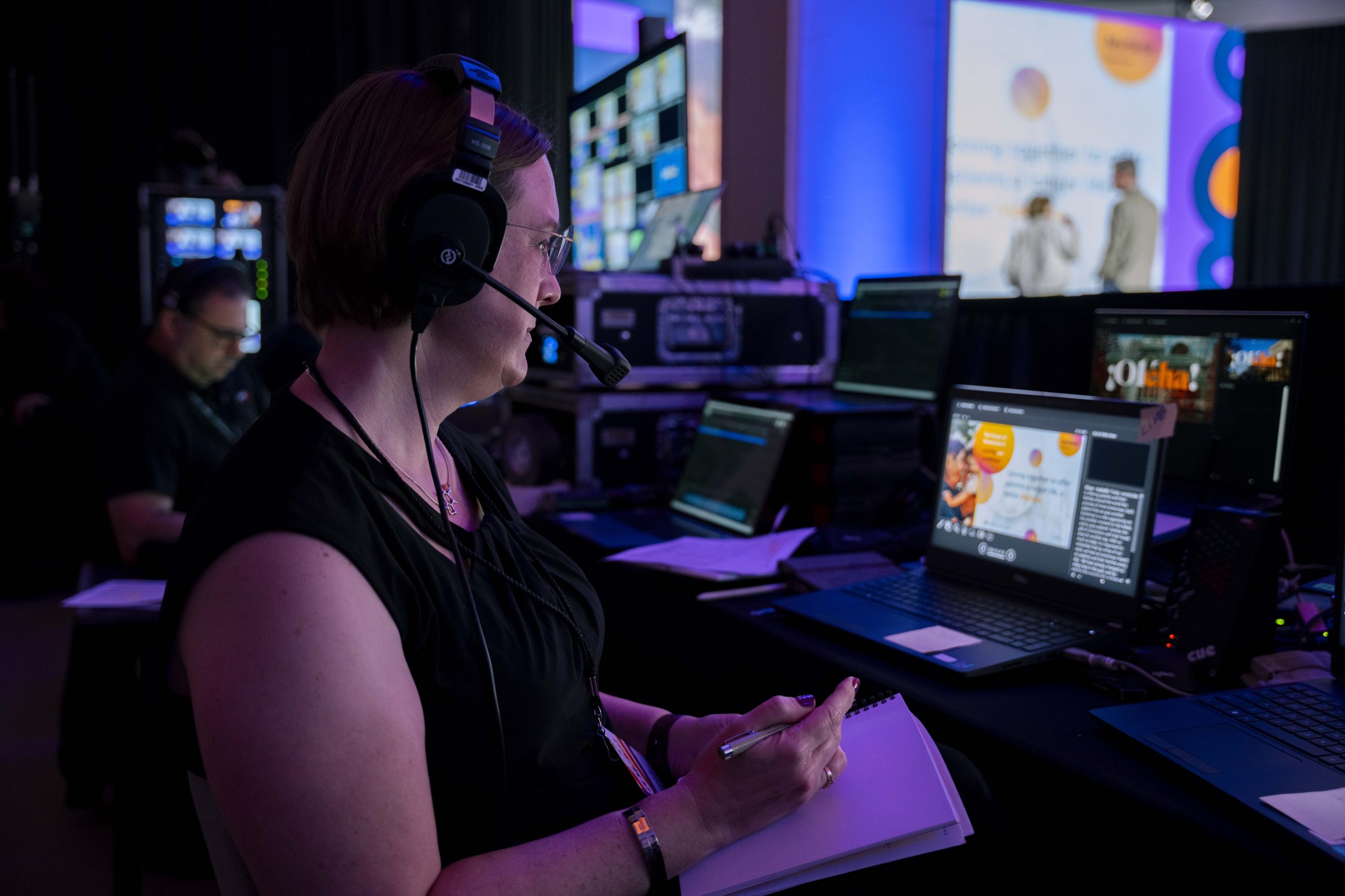 A female, Brella event management agency technician takes notes during a live corporate event rehearsal.
