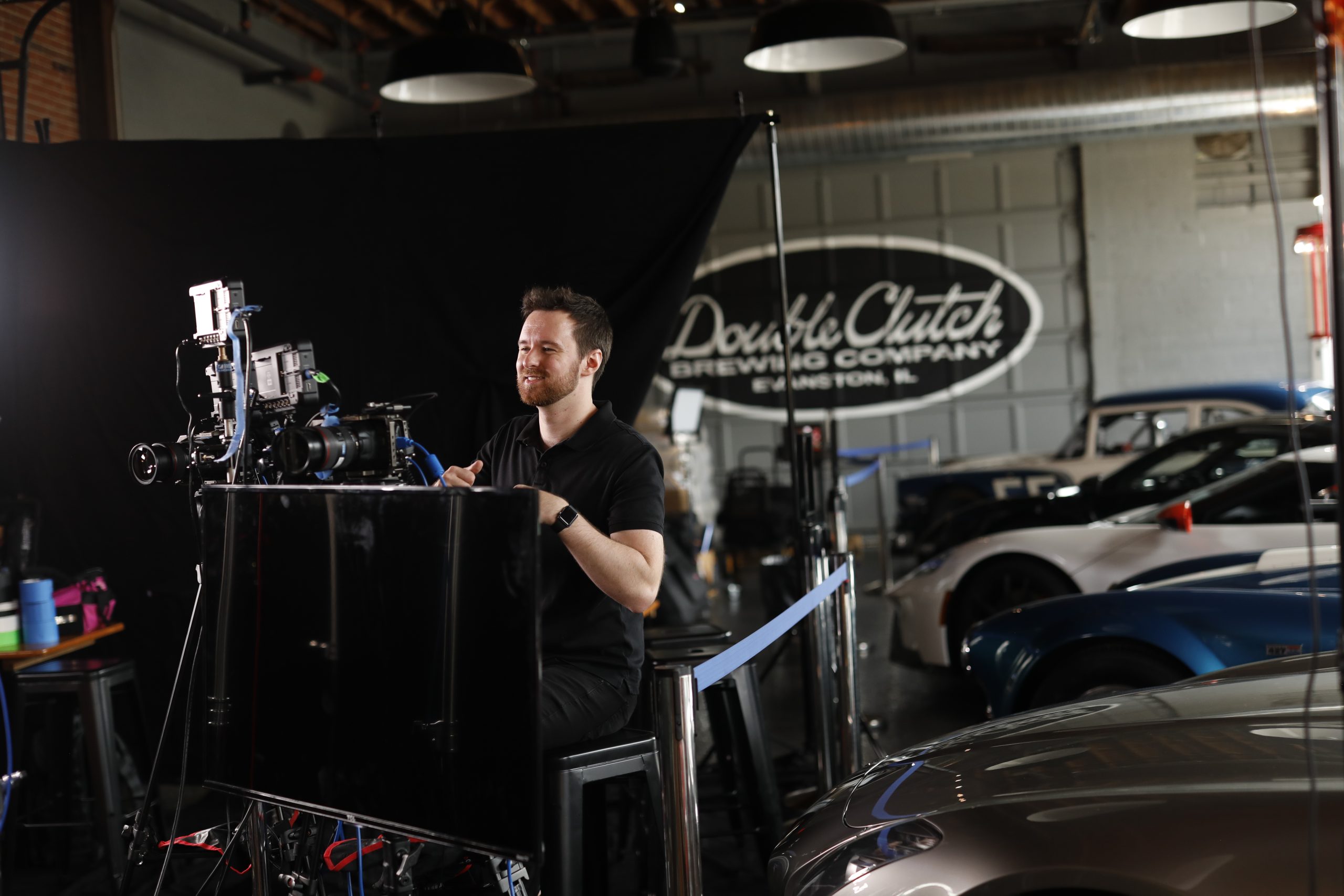Smiling, Brella Productions video producer operates a camera during a shoot on location in a classic car showroom.